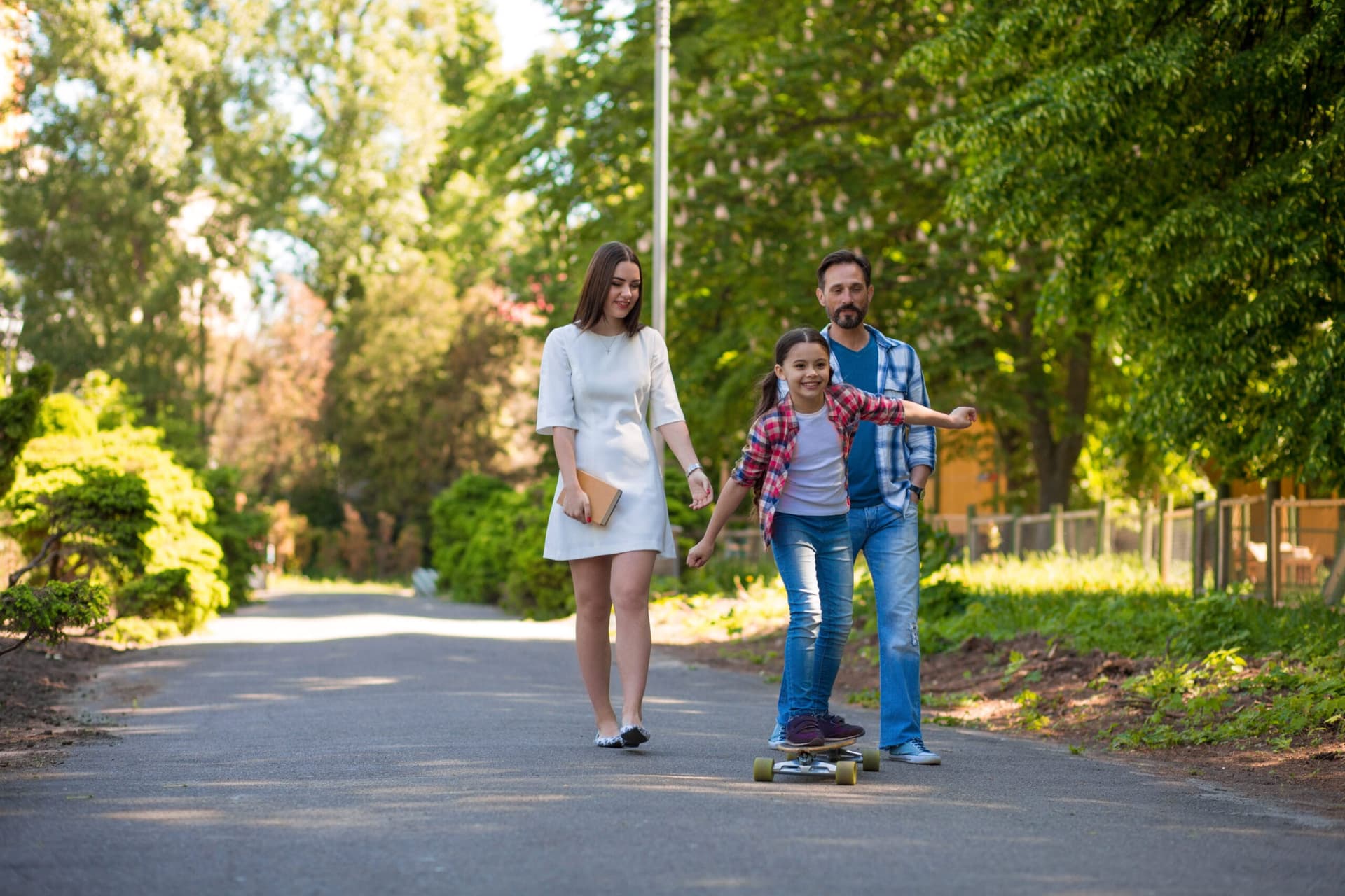 Girl Teenager Is Riding A Skateboard In The City Park. Parents Watching Her.