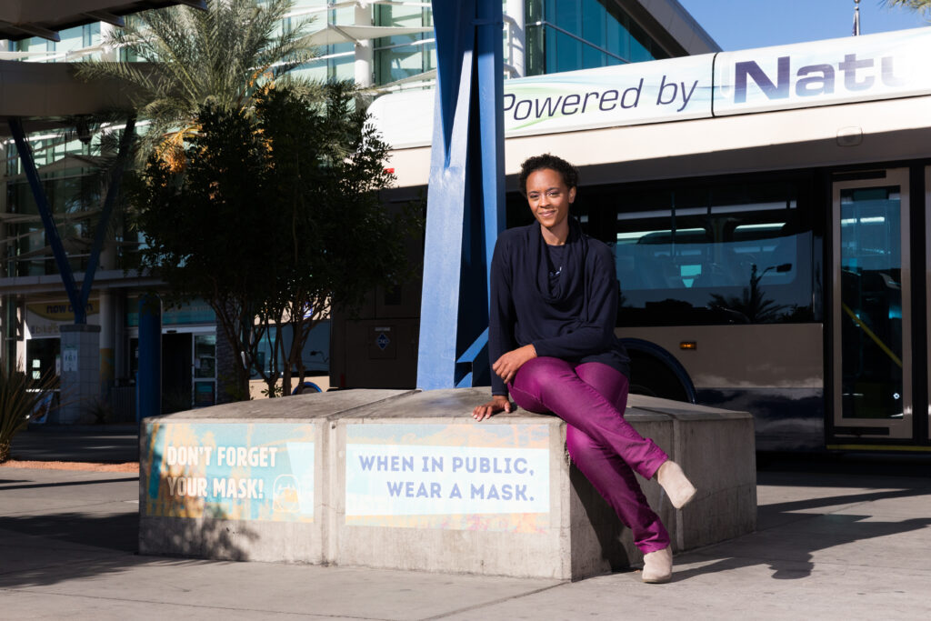 Image of a person sitting on a concrete seating area. Attached to the concrete seating area is signage that reads “DON’T FORGET YOUR MASK!” and “When in public, wear a mask.”