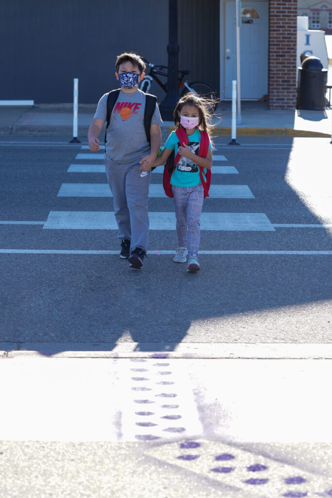 Image of two young people walking on a crosswalk towards a set of stenciled purple footprints on the sidewalk.