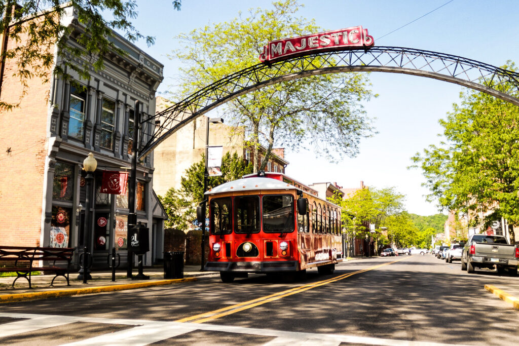 Red transit trolley with historic design passes through an arch that reads 