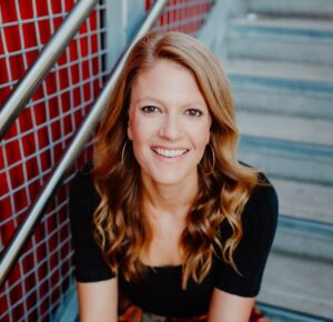 A headshot of investigative journalist Megan Kimble sitting on gray stairs red tiled walls