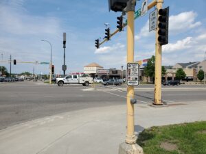 Photograph of A wide roadway with a narrow crosswalk and traffic signals with beg buttons for pedestrians to push
