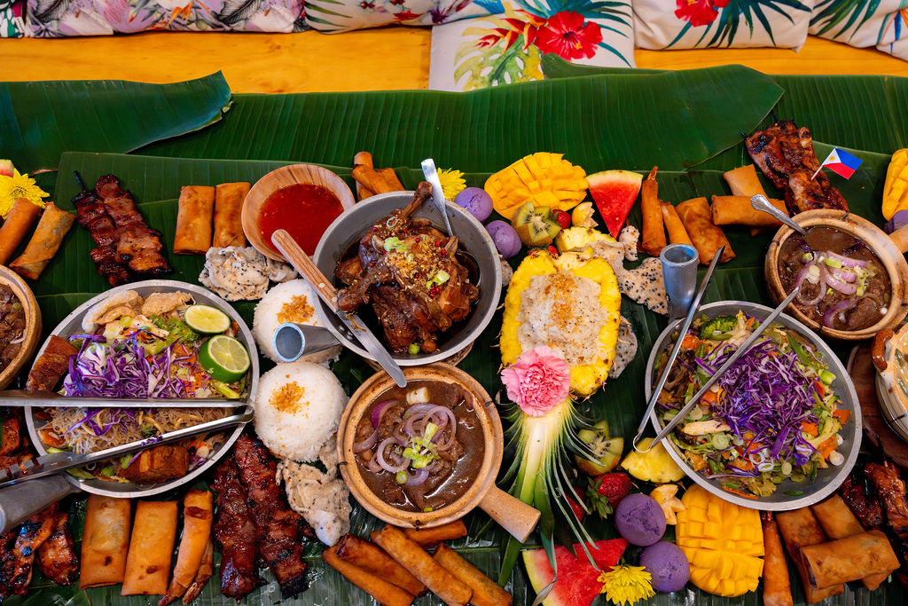 A table at the restaurant Kamayan ATL displaying a variety of Filipino dishes laid out on banana leaves in the kamayan style of communal dining, which is Tagalog for 