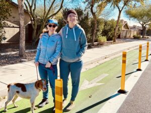 Hannah stands with her dog and a neighbor posing for a photo in a bike land. 