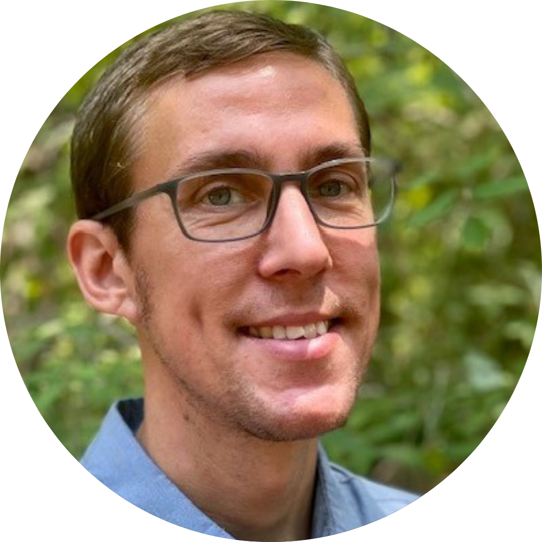 Seth LaJeunesse's headshot, short brown hair and glasses with a blue collared shirt, with leaves in the background