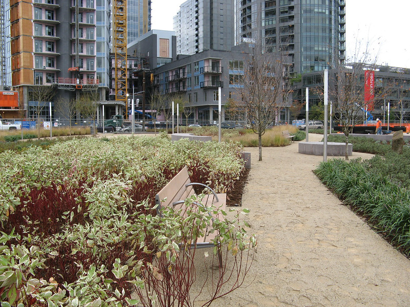 A sidewalk and greenspace replaces what was once a brownfield. Apartments rise in the distance.