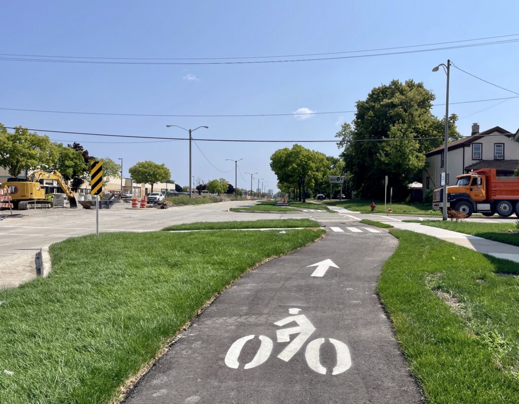 A bike trail curves through a patch of grass adjacent to a sidewalk