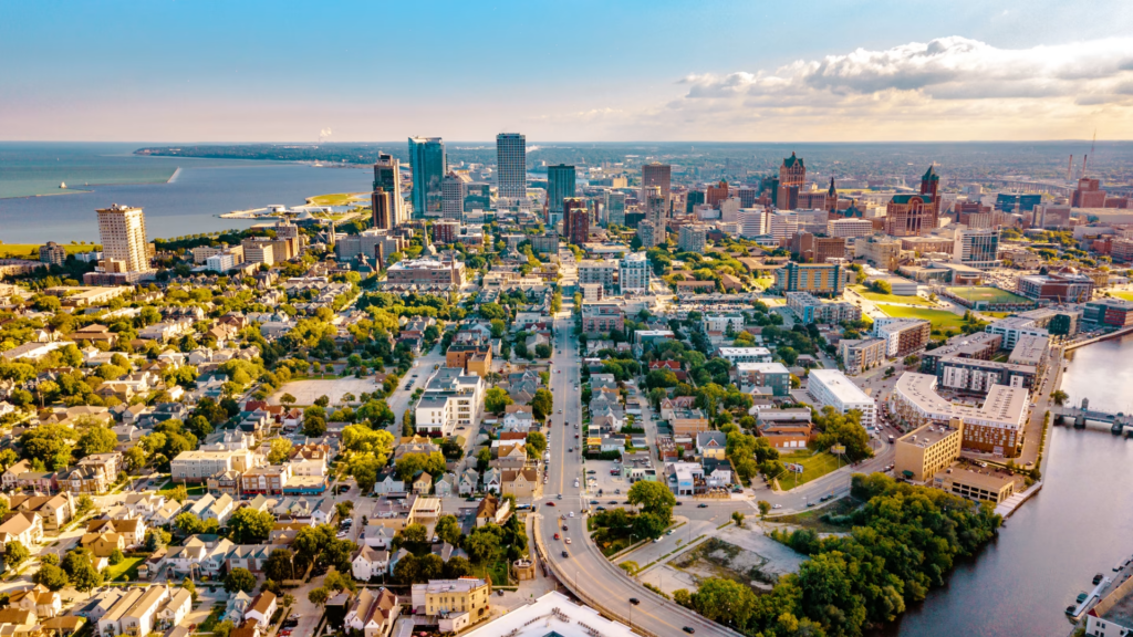 The City of Milwaukee is shown with two bodies of water on either side. A major roadway crosses the river and transports drivers downtown. Smaller, tree-lined streets are lined with houses and small businesses.
