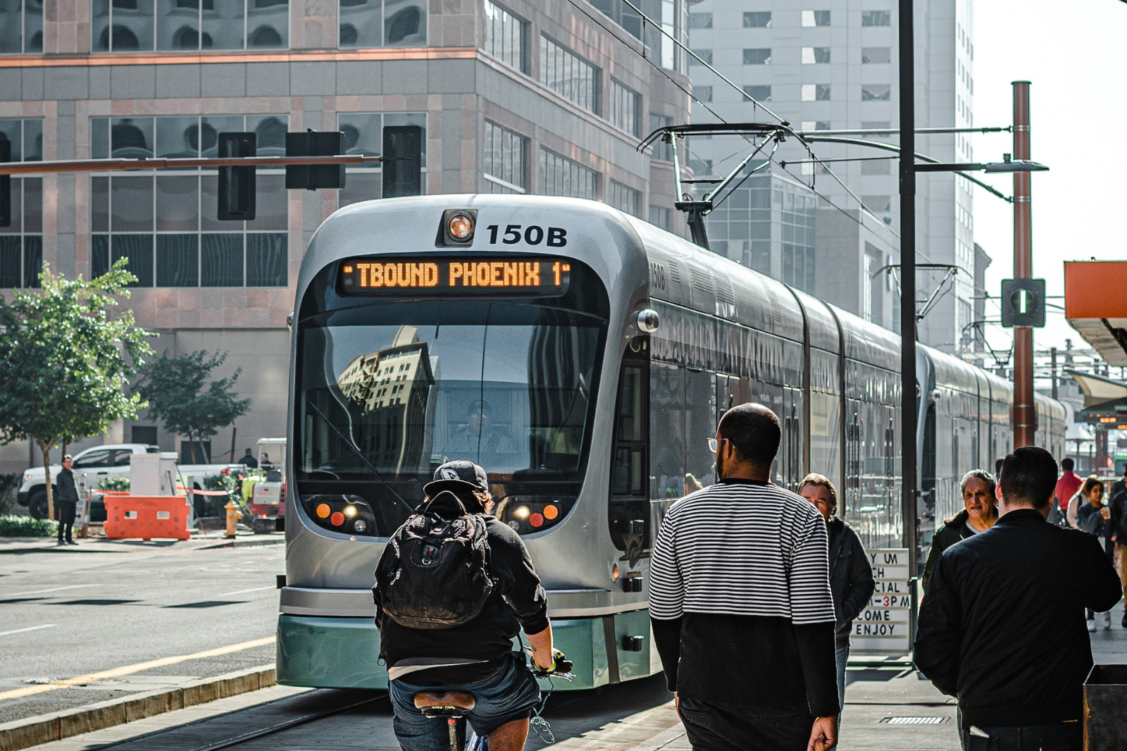 A t-bound rail car in Phoenix, Arizona reaches a stop by a sidewalk filled with people walking and biking