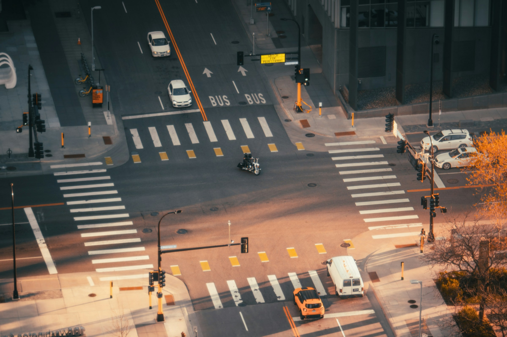Cars line up behind crosswalks at a freshly painted Minnesota intersection. A motorcyclist is able to turn left without facing oncoming traffic.