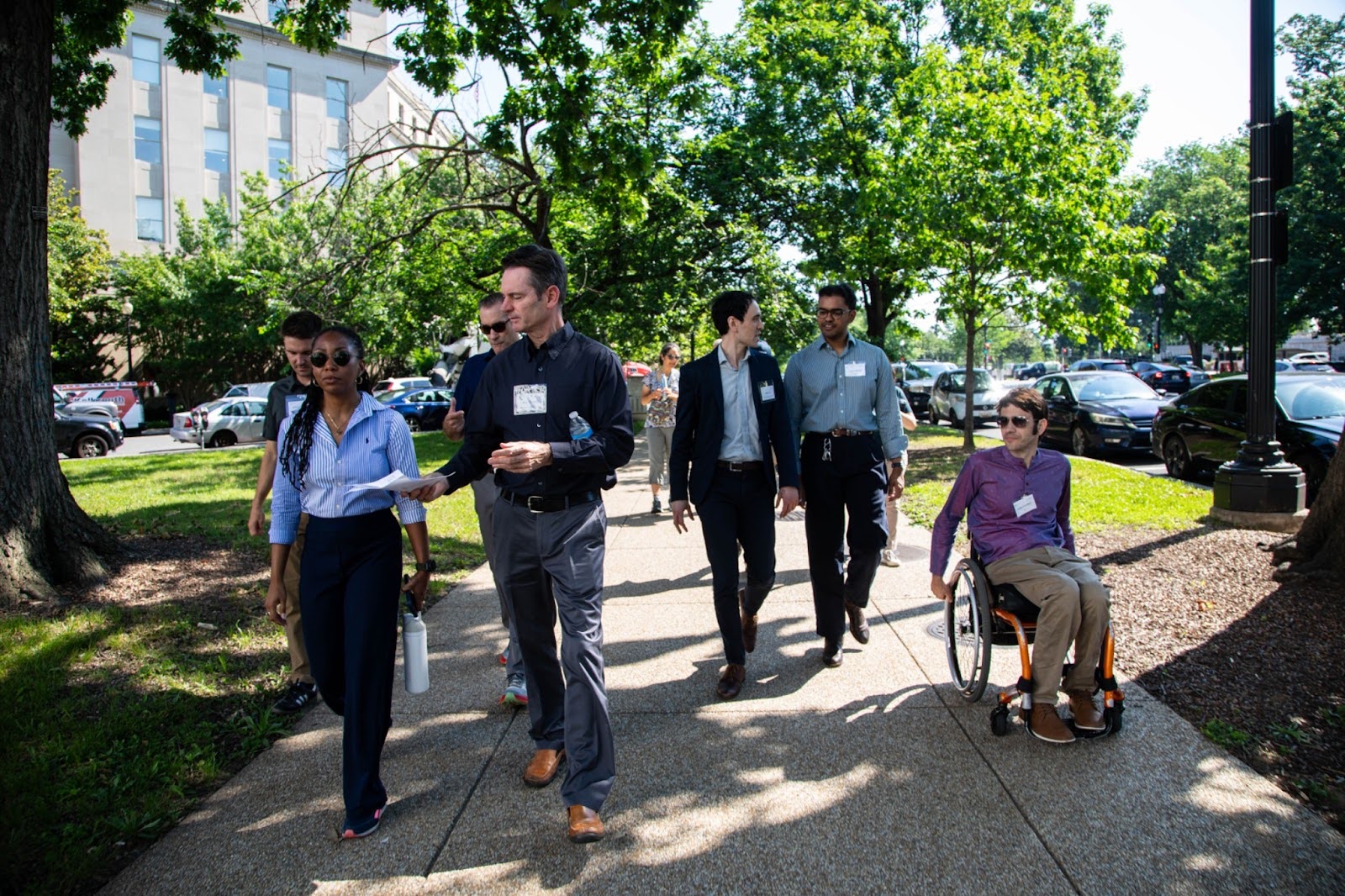 A group of people walk down a tree-lined sidewalk on a walking tour in Massachusetts
