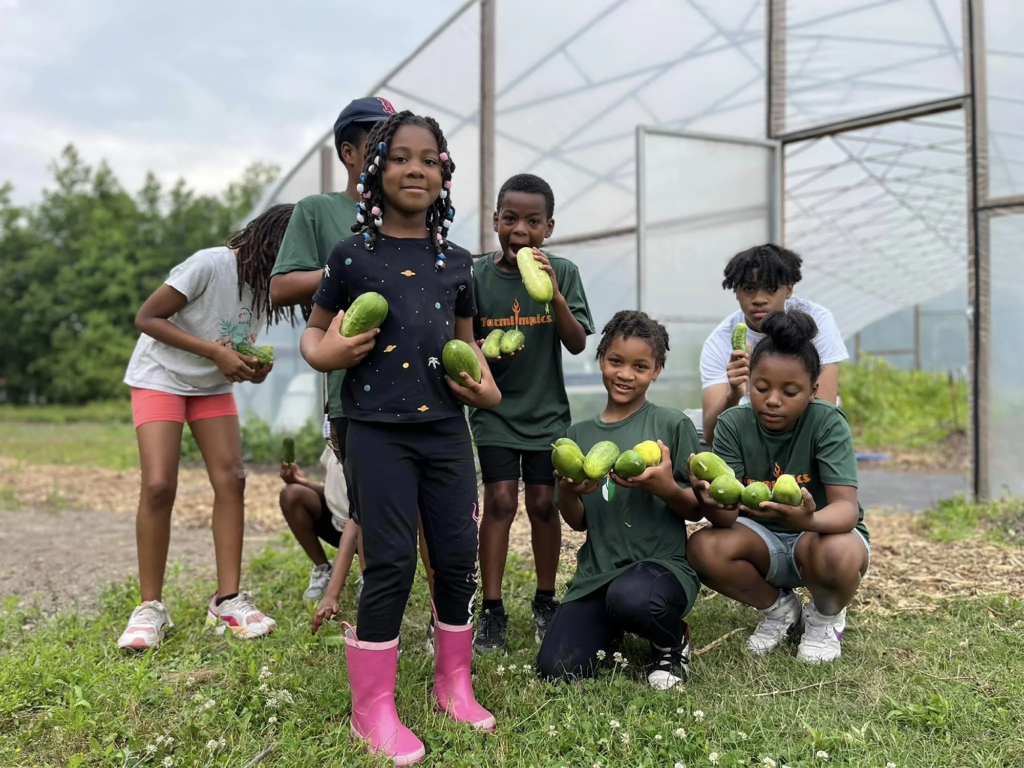 A group of Black children excitedly showing off cucumbers grown in The Tarboro/Edgecombe Community Demonstration Garden