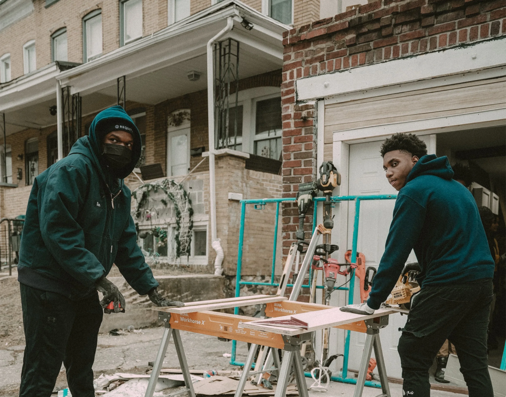 Two teenagers engaged in construction in front of a row home