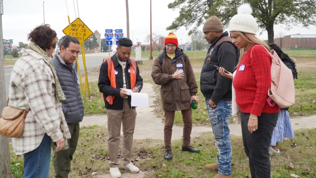 A small group stands in a circle on a sidewalk during a March walk audit of the street.